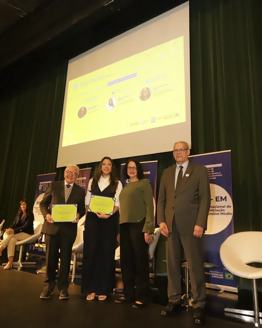 Késsia Souza Santos on the PUC-SP stage holding her certificate, next to authorities from CNPq, MCTI and ABC