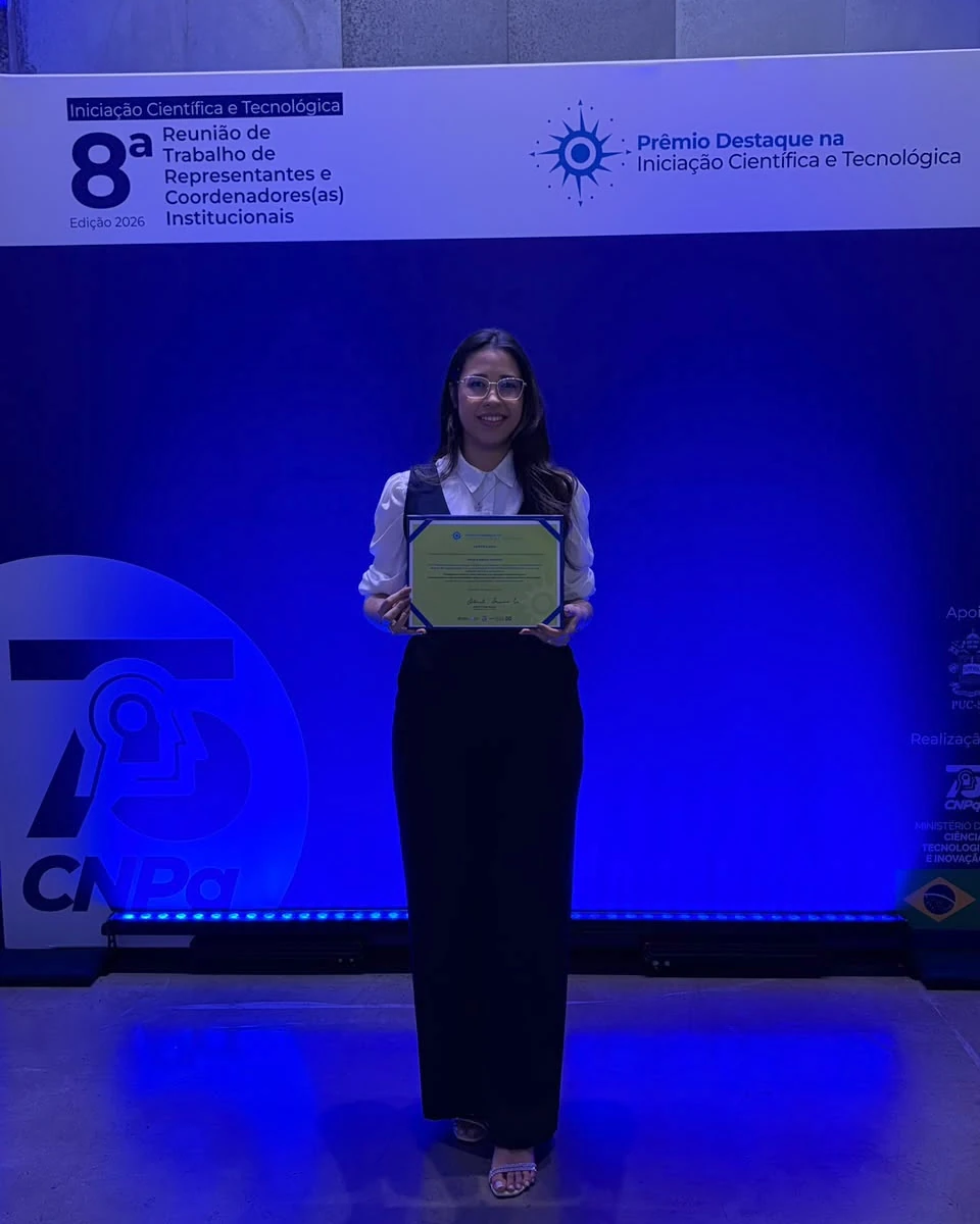 Késsia Souza Santos with her certificate in front of the Highlight Award panel