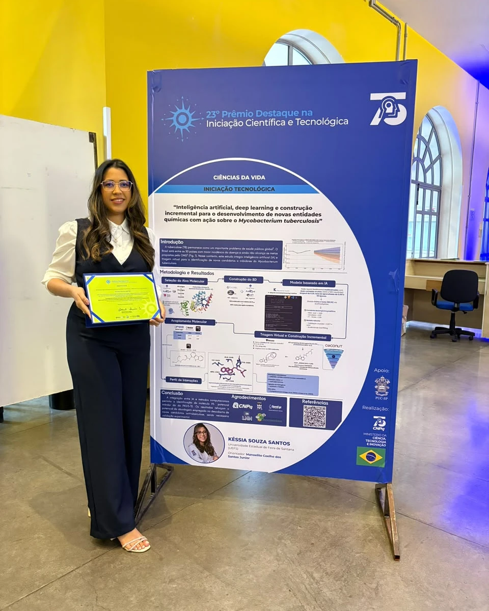 Késsia Souza Santos holding her certificate next to the poster of the award-winning work