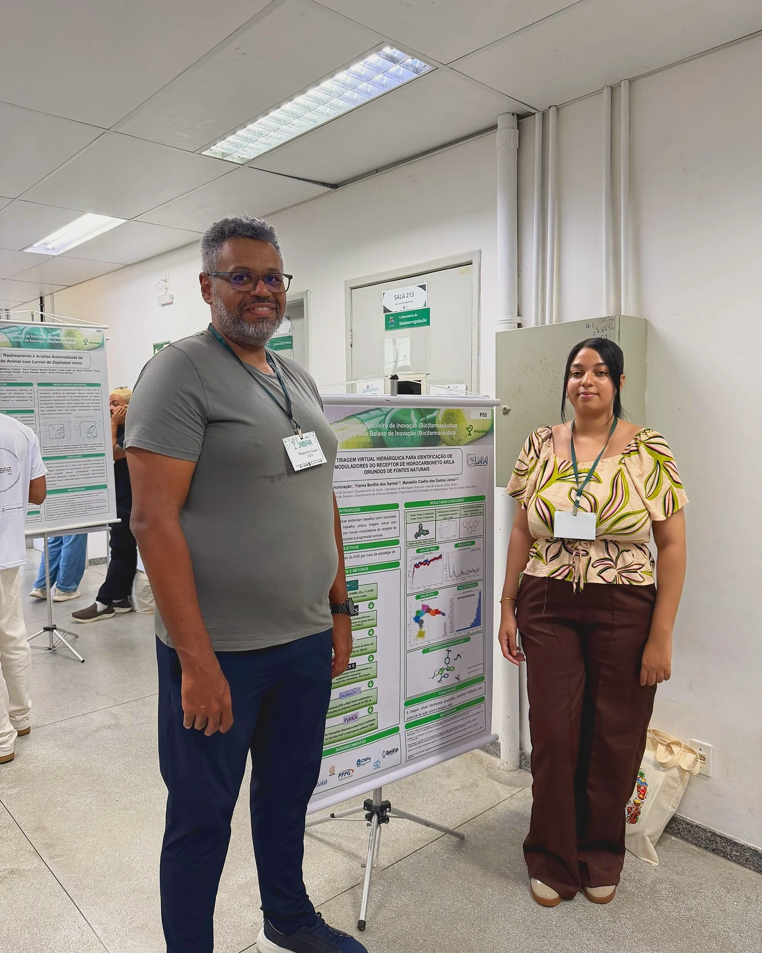 Manoelito Junior e Caroline Anunciação ao lado do pôster P05